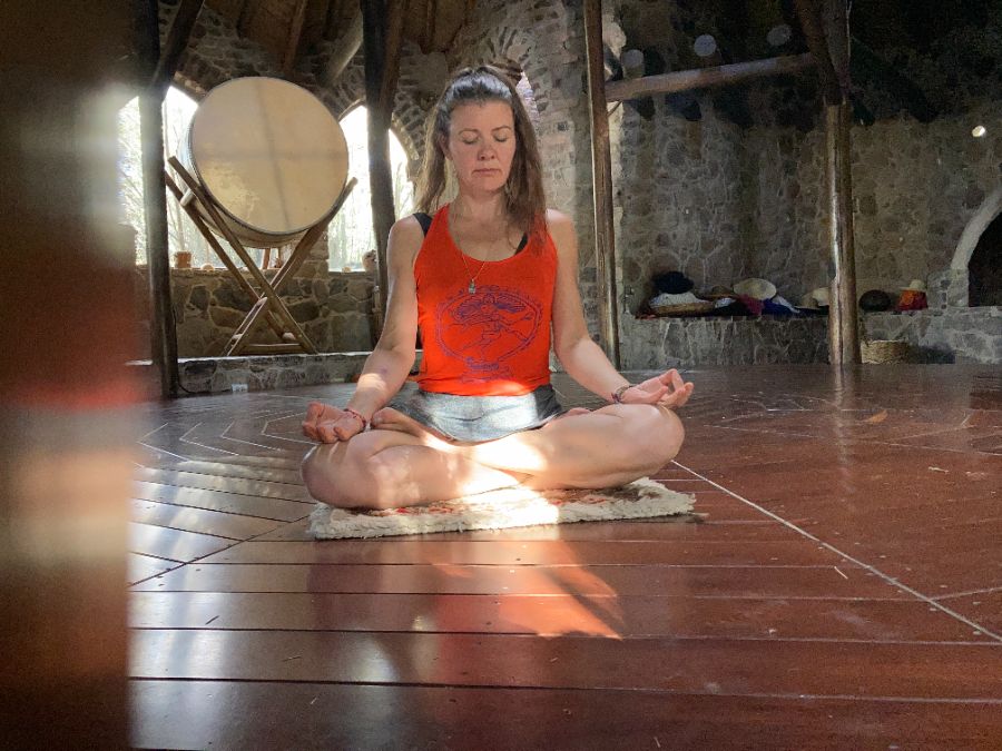 Simone sitzt in Meditation in einer offenen Holzhalle im warmen Morgenlicht