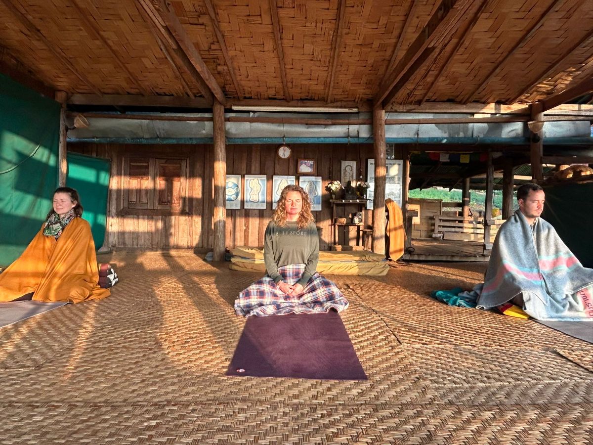 Gemeinsame Meditation in einer offenen Holzhalle im Morgenlicht, Simone in der Mitte